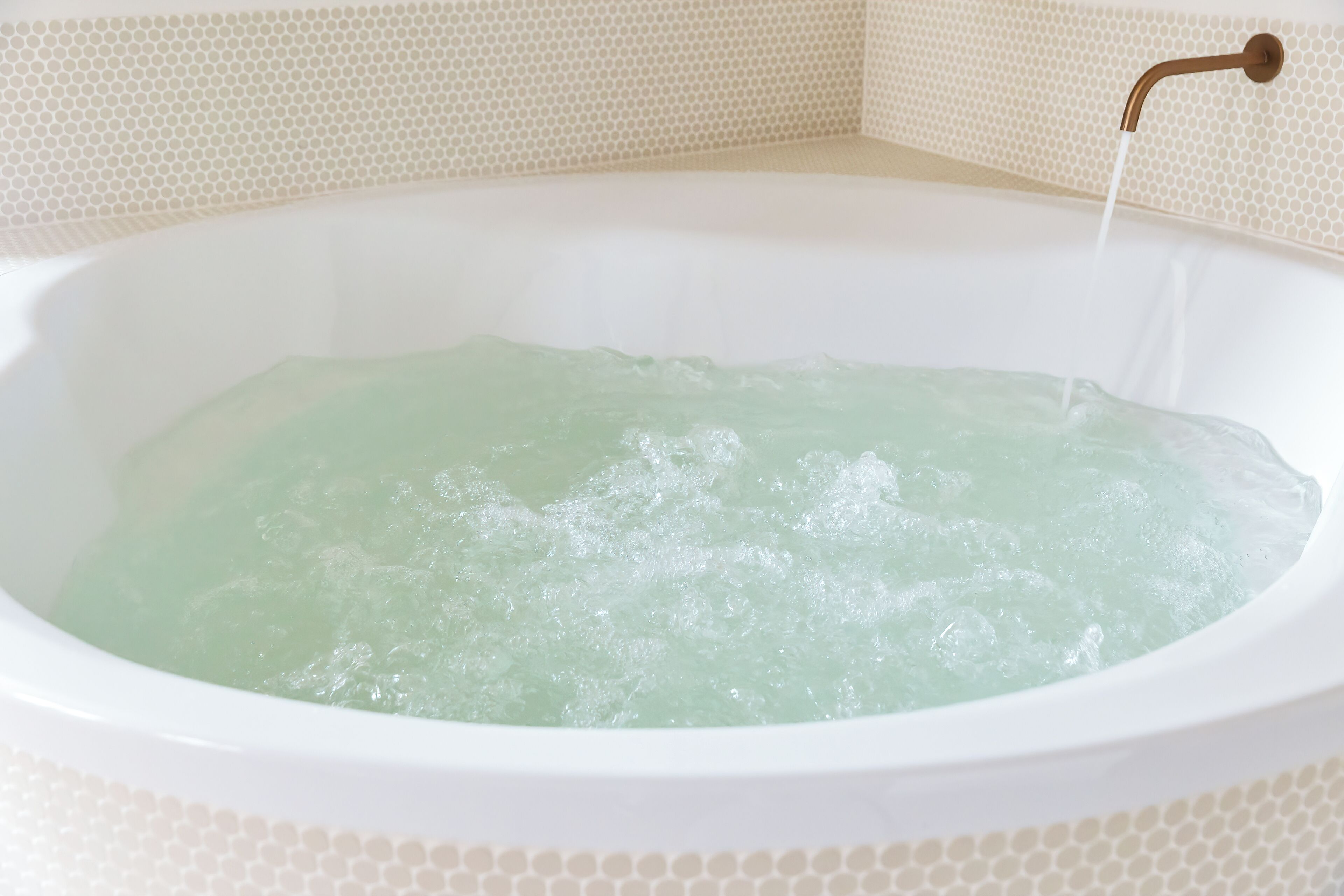 A bathtub filled with clear water, a faucet, and a tiled wall with a hexagonal pattern.