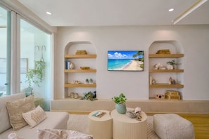 A modern living room with a large flat-screen TV, wooden shelves, and a comfortable seating area. - ®{Marbella~LUX~Sunsets} Beachfront+Pool+Families (Playa Juan Dolio)
