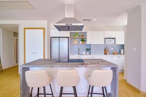 A modern kitchen with a central island, bar stools, a stainless steel range hood, and built-in appliances. - ®{Marbella~LUX~Sunsets} Beachfront+Pool+Families (Playa Juan Dolio)
