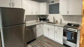 Una cocina con armarios blancos, un refrigerador de acero inoxidable, un microondas, un lavavajillas, un fregadero y una estufa.