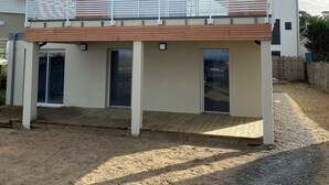 Ein modernes, zweistöckiges Haus mit Holzfassade, einem Balkon mit weißen Geländern und einem Schotterweg.