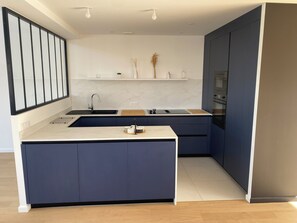 Une cuisine moderne dotée d’un îlot central, d’un four encastré et d’un pare-feu en marbre blanc.