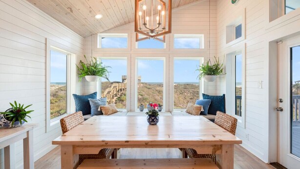 Un interior de madera con una gran mesa de comedor, varias ventanas y plantas en macetas.