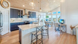 Una cocina moderna con armarios azul marino, una isla grande con taburetes y vistas al océano a través de amplias ventanas.