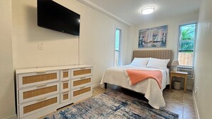 A bedroom with a bed, a dresser, a television mounted on the wall, and a painting above the bed. - SunShell 2 - Steps from Sand (Fort Myers)