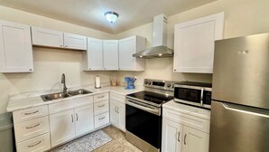 A kitchen with white cabinets, a stainless steel refrigerator, a double oven, a microwave, and a sink. - SunShell 2 - Steps from Sand (Fort Myers)