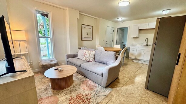A compact living space with a sofa, coffee table, and a kitchen area including a refrigerator and cabinets. - SunShell 2 - Steps from Sand (Fort Myers)
