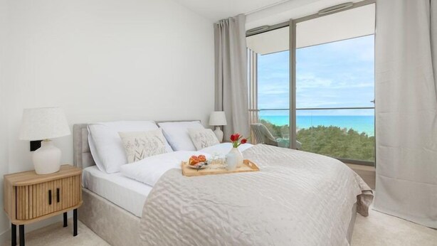 A modern bedroom with a large bed, a nightstand, a lamp, and a tray with flowers.