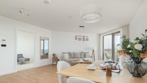 A modern living room with a wooden dining table, white sofas, and a large window.