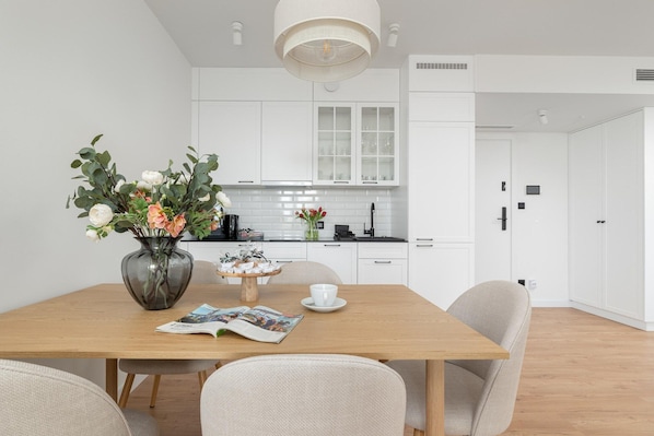 A modern kitchen with white cabinets, a wooden dining table, and a vase with flowers.