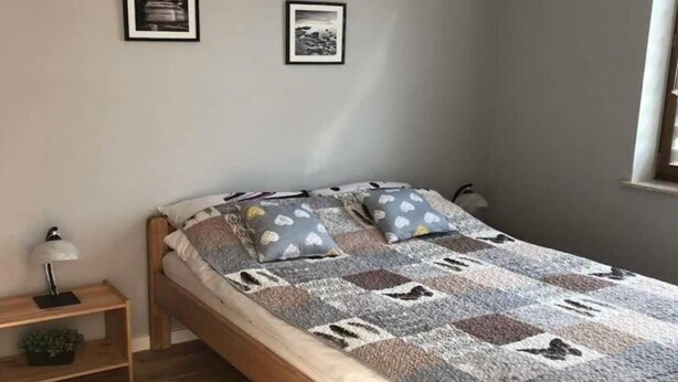 Un dormitorio con cama, almohadas, mesita de noche y lámpara.