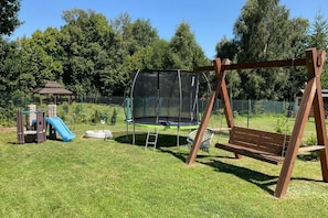 Ein Spielplatz mit Schaukel, Rutsche und Trampolin.
