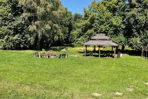 Ein Pavillon mit Dach, umgeben von einer Wiese und Bäumen.