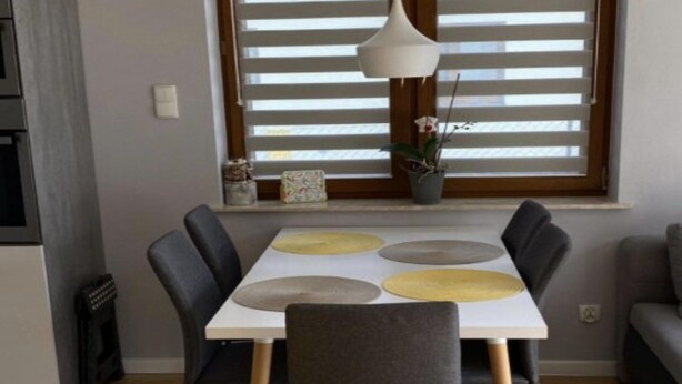 Un coin repas comprenant une table, des chaises et une fenêtre avec des stores.