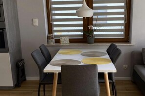 A dining area with a table, chairs, and a window with blinds. - Holiday home with a large garden and playground (Debina)