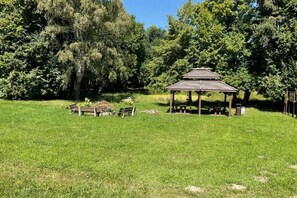 A gazebo with a roof, surrounded by a grassy field and trees. - Holiday home with a large garden and playground (Debina)