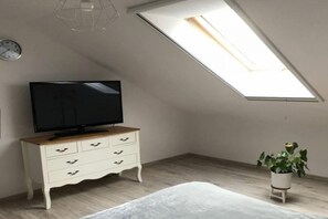 A room with a sloped ceiling, a television on a wooden dresser, a bed, and a potted plant. - Holiday home with a large garden and playground (Debina)