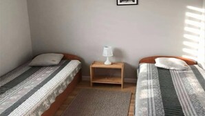 A room with two single beds, a small wooden nightstand with a lamp, and a framed picture on the wall. - Holiday home, large garden with gazebo, playground (Debina)