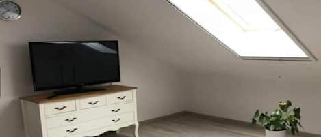 Un dormitorio con techo inclinado, un televisor sobre una cómoda, una cama y una planta en maceta.