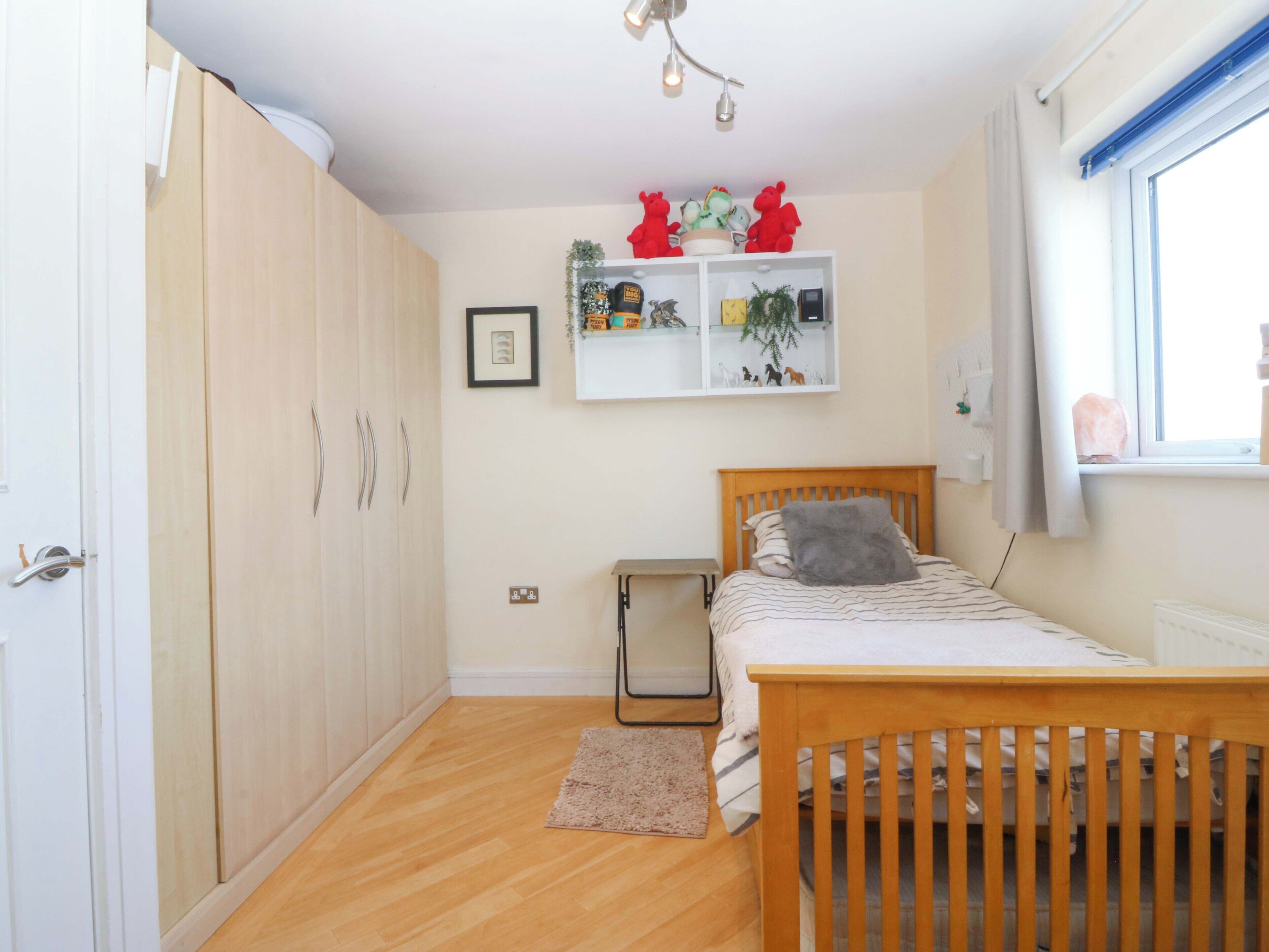 Une chambre à coucher avec un lit en bois, une armoire, une étagère ornée d’objets décoratifs et une fenêtre.
