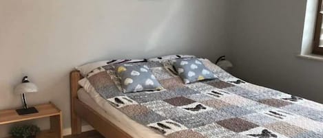 Un dormitorio con cama, almohadas, mesita de noche y lámpara.