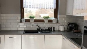 A modern kitchen with white cabinets, a stainless steel sink, and a window with blinds. - Holiday home, large garden with playground, gazebo (Debina)