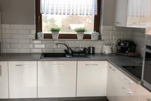 Eine moderne Küche mit weißen Schränken, einer Edelstahl-Spüle und einem Fenster mit Jalousien.