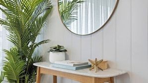 A wooden console table with a white marble top, a potted plant, a mirror, and a few books. - Oceans 14th Beachfront Resort style Living (Broadbeach)