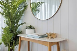 A wooden console table with a white marble top, a potted plant, a mirror, and a few books. - Oceans 14th Beachfront Resort style Living (Broadbeach)