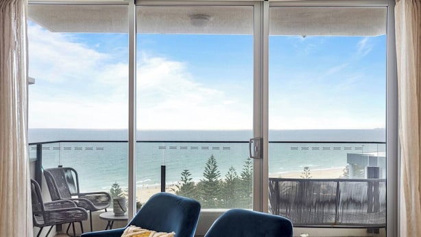 A balcony with two blue chairs, a table, and a view of the ocean. - Oceans 14th Beachfront Resort style Living (Broadbeach)