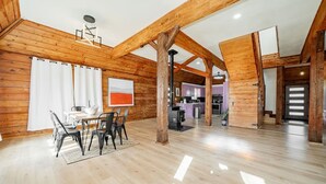 Ein geräumiger Raum mit Holzwänden und hoher Decke, mit einer Essecke mit Tisch und Stühlen, einer Küche im Hintergrund und einer Treppe, die zu einer weiteren Ebene führt.