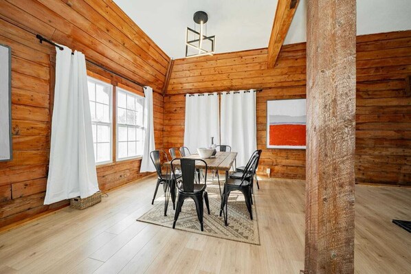 A wooden cabin interior with a dining area, large windows, and a ceiling light fixture. - Serene peaceful Purple Pyramid Escape 2 Bed 2 Bath (Van Alstyne)