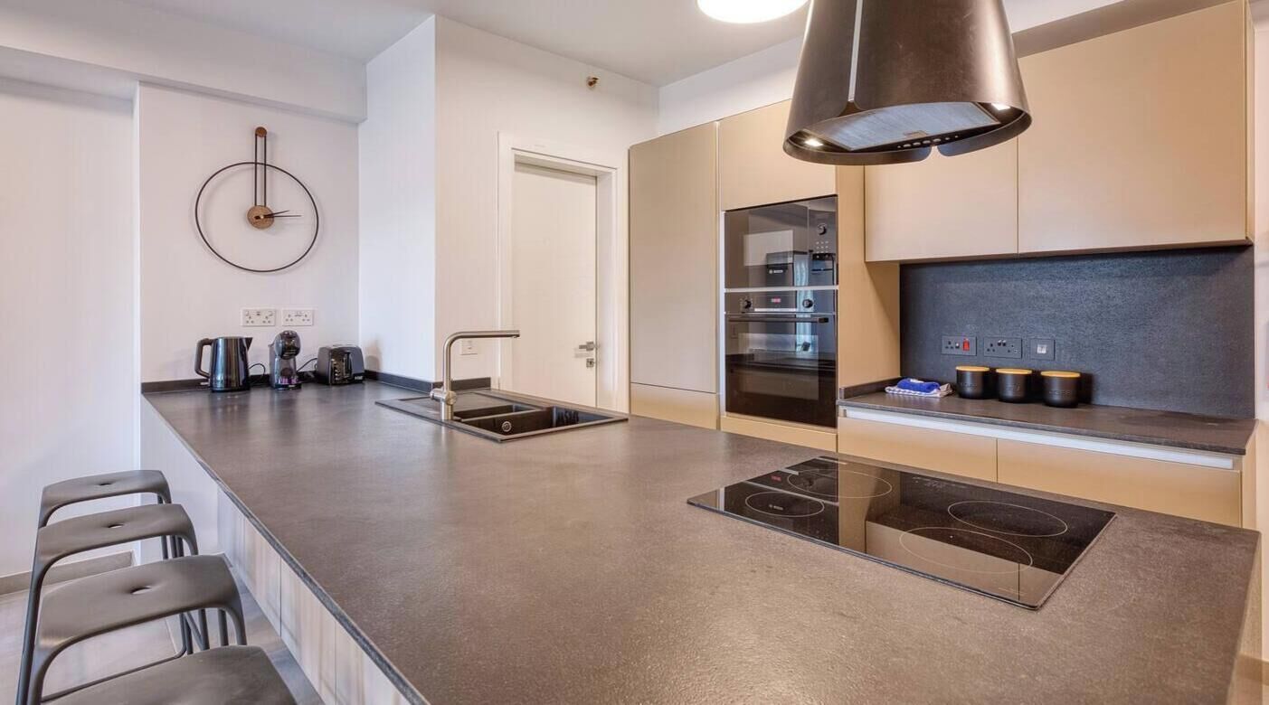 Cuina moderna amb una illa central, forn de forn i rellotge penjat a la paret.