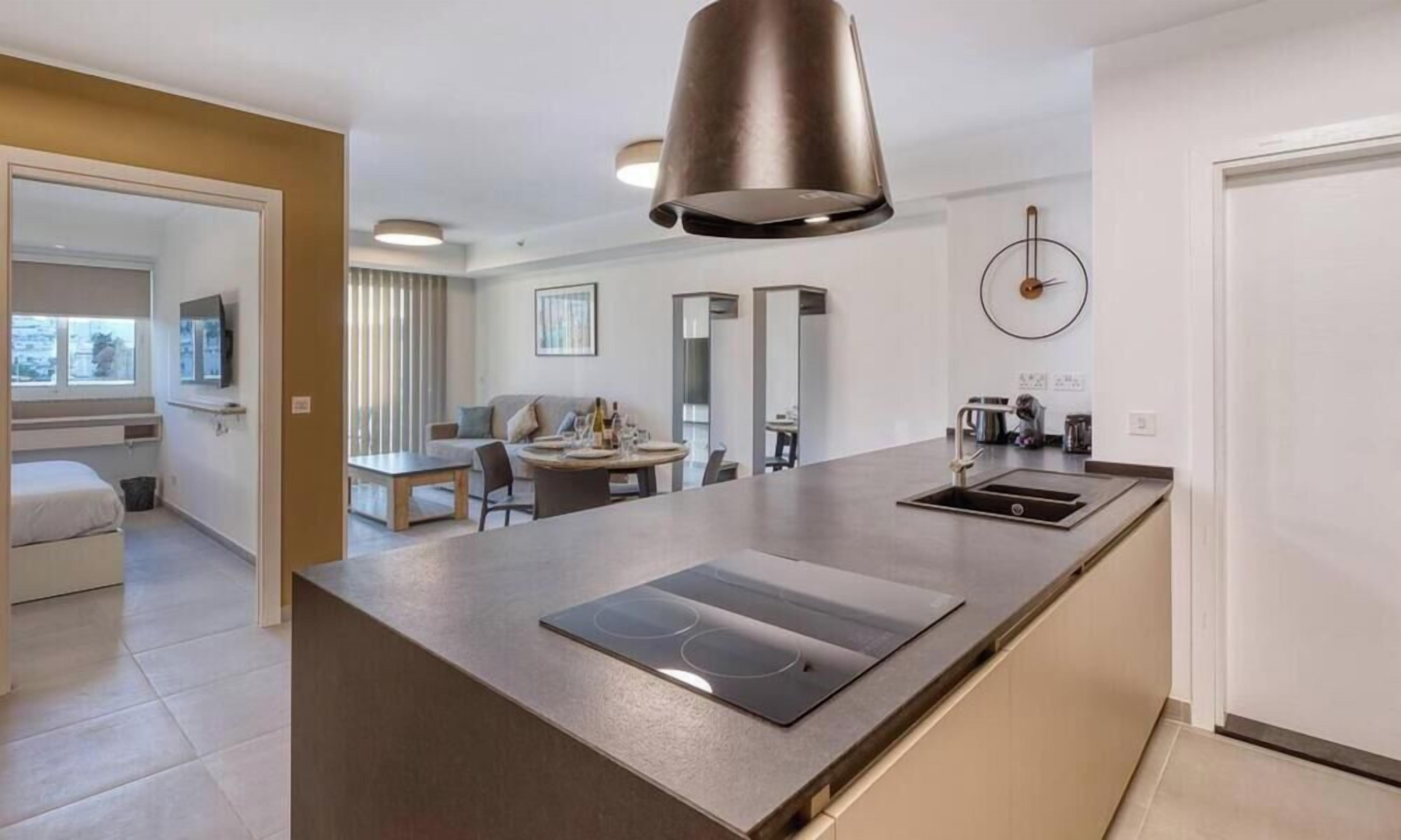 A modern kitchen with a central island, a dining area with a table and chairs, and a living space with a sofa and a TV.