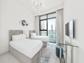 Ein modernes Hotelzimmer mit einem großen Bett, einem kleineren Bett, einem Fernseher und Blick auf die Stadt durch das Fenster.