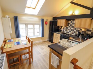 A compact kitchen with a dining area, a black refrigerator, a stove, and a window with curtains. - 3 The Old Drill Hall (Alford)