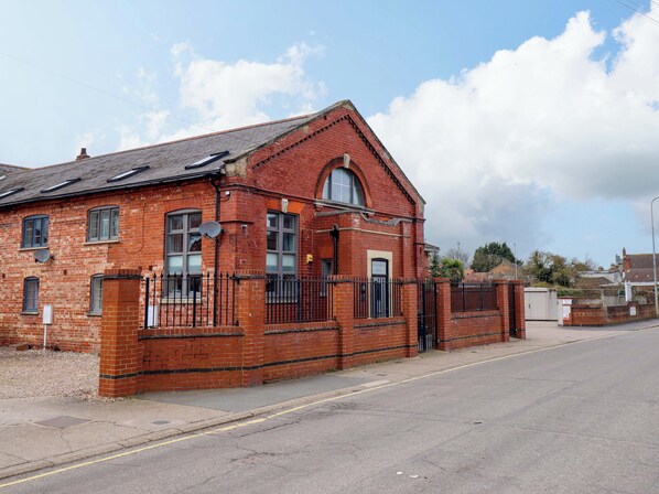 A red brick building with a pitched roof, a gated entrance, and a small satellite dish on the roof. - 3 The Old Drill Hall (Alford)