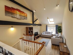 A spacious living area with a high ceiling, a staircase with wooden railings, a large window with curtains, and a flat-screen TV.