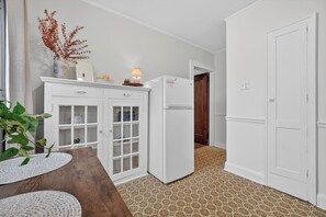 Eine kleine Küche mit weißen Schränken, einem Kühlschrank und einem Esstisch mit einer Pflanze.