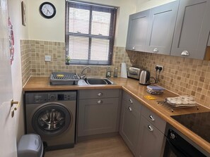 A compact kitchen with a washing machine, a toaster, and a sink. - Cedarfell, a ground floor centrally located apartment in Keswick (Keswick)