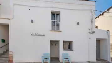 A building with a sign reading 'Via Roma 50' and two blue chairs outside.