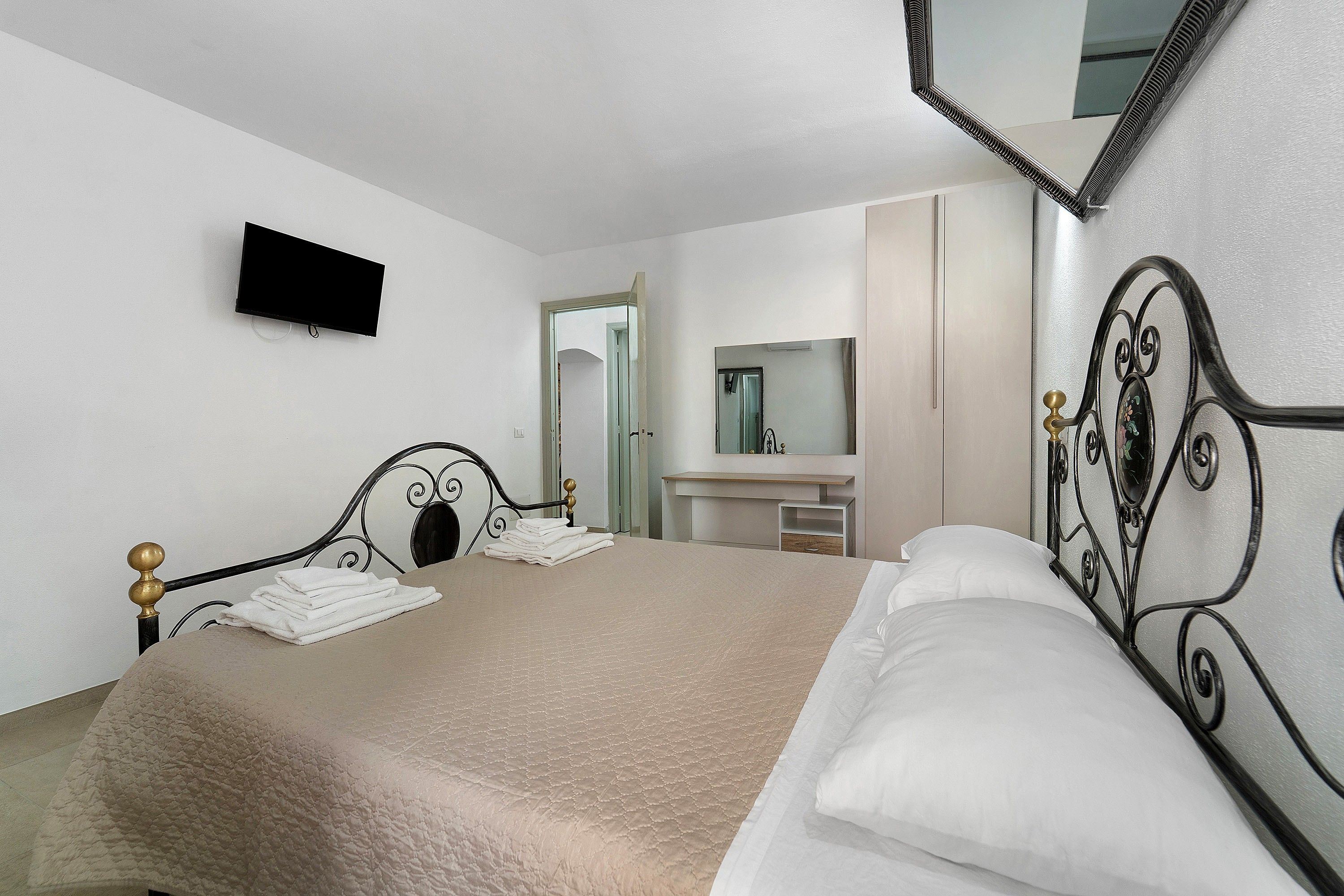 Een hotelkamer met een bed, een wandtelevisie, een badkamer met spiegel en een deur naar een andere kamer.