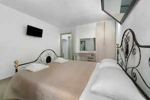 Hotellihuone, jossa on sänky, seinälle asennettu taulutelevisio, kylpyhuone peilillä sekä ovi, joka johtaa toiseen huoneeseen.