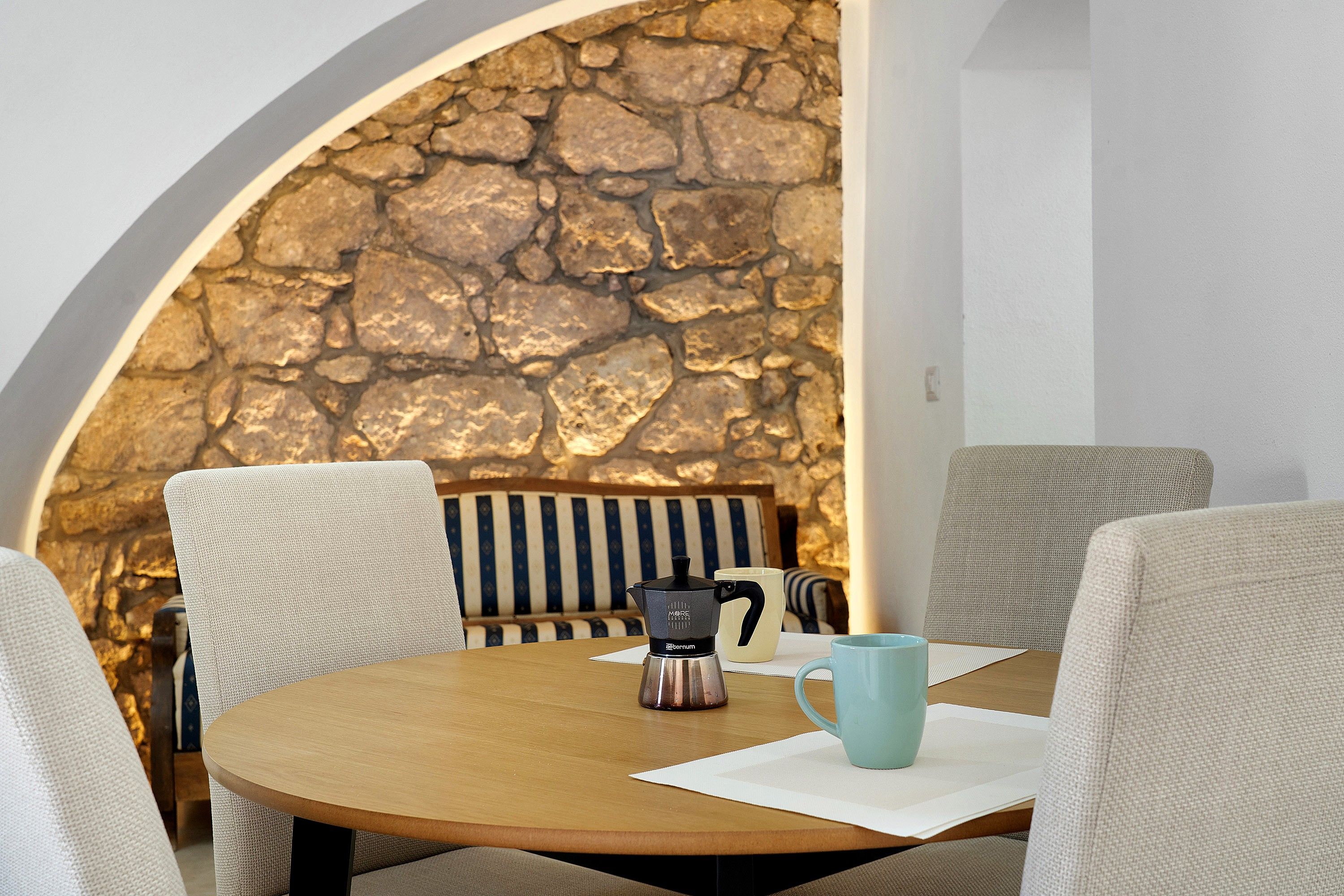 Una mesa de madera redonda con un fondo de pared de piedra, una cafetera y dos tazas.