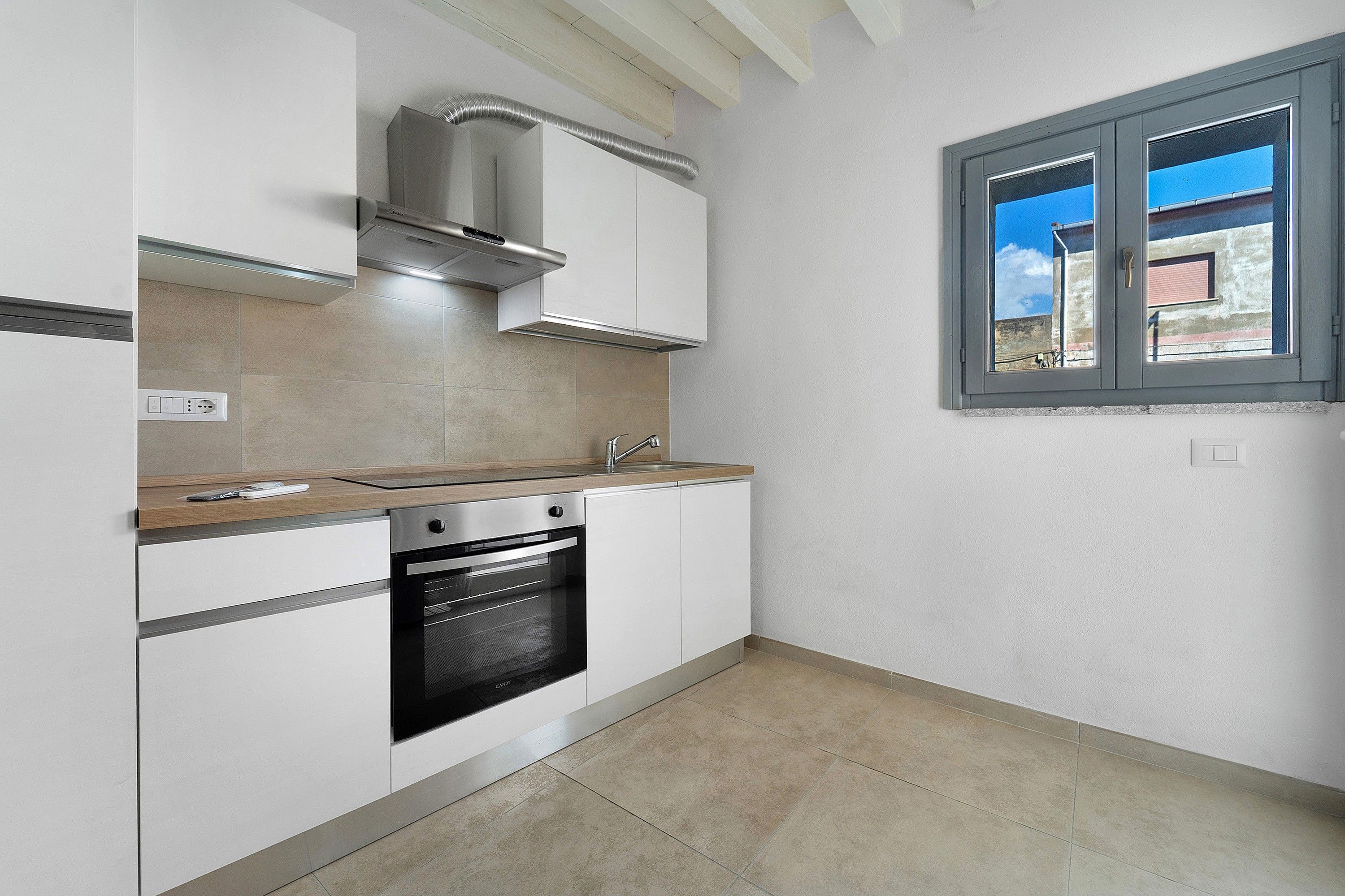 A modern kitchen with a built-in oven, a window with a view, and a light-colored tiled floor.