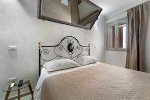 Un lit bien fait, recouvert d’une courtepointe matelassée, une table de chevet avec un plateau en verre et un miroir fixé au mur au-dessus.