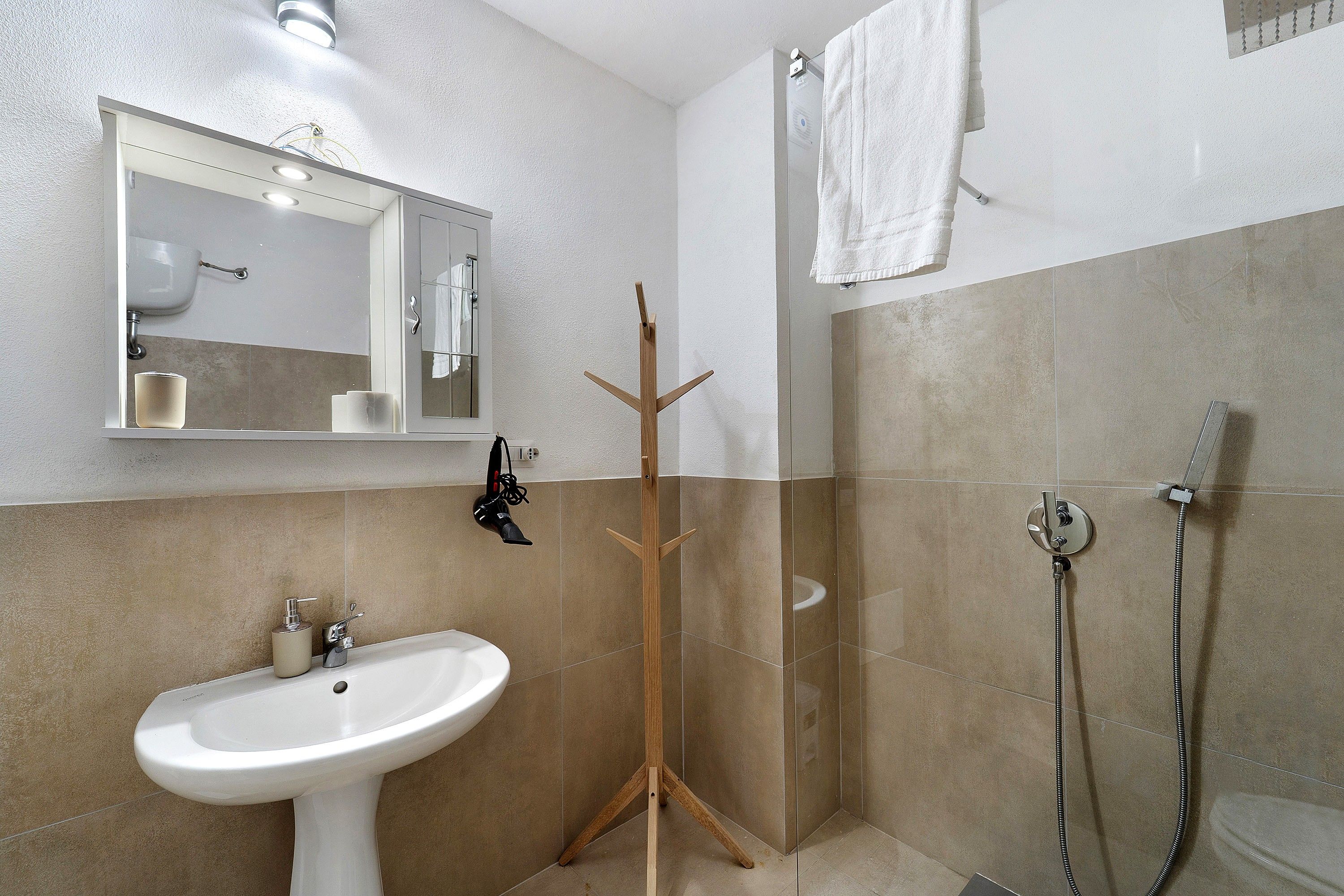 A bathroom with a white sink, a mirror, a towel rack, and a shower area.