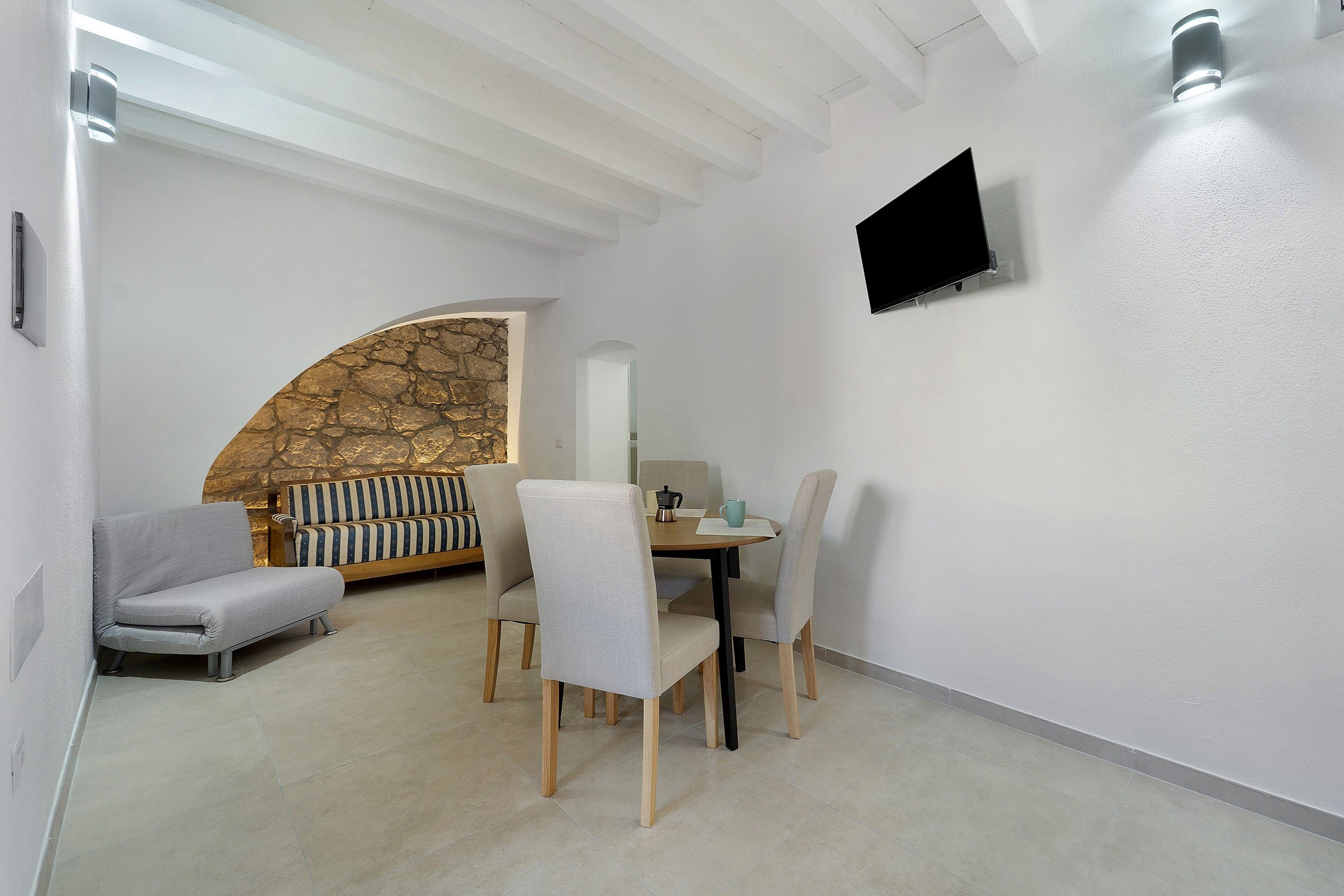 A modern dining area with a round table, four chairs, and a sofa with striped cushions.