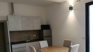 Et lille køkken med spisebord og stole, indbygget ovn samt en vægmonteret lampe.