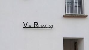 En bygnings facade med et skilt, der viser 'Via Roma 50', og et vindue med gelænder.